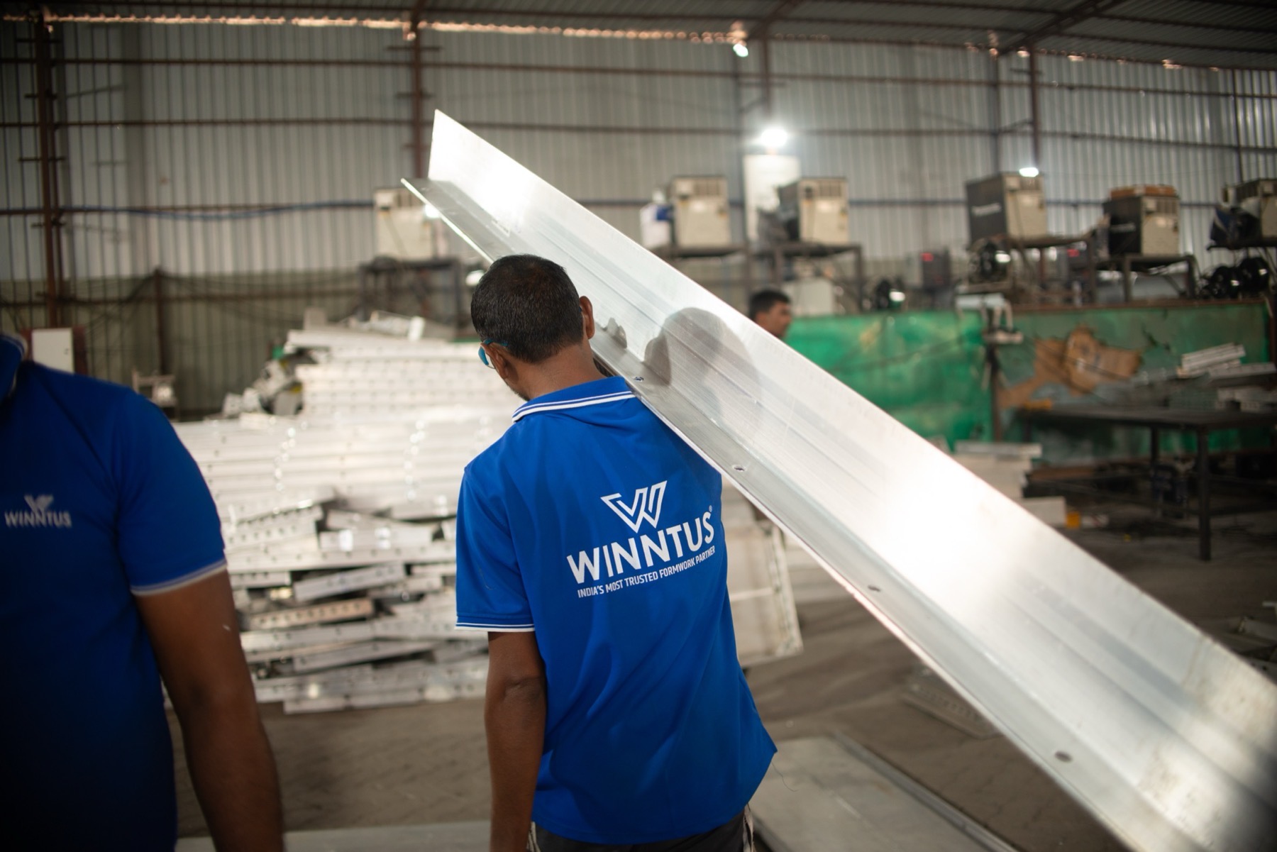 A worker carrying a long aluminium section across the shop