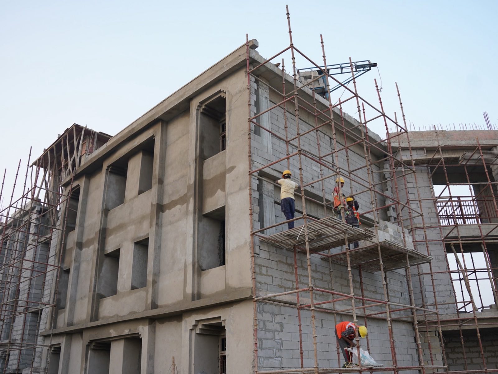 Two workers in orange uniforms inside an unfinished concrete frame